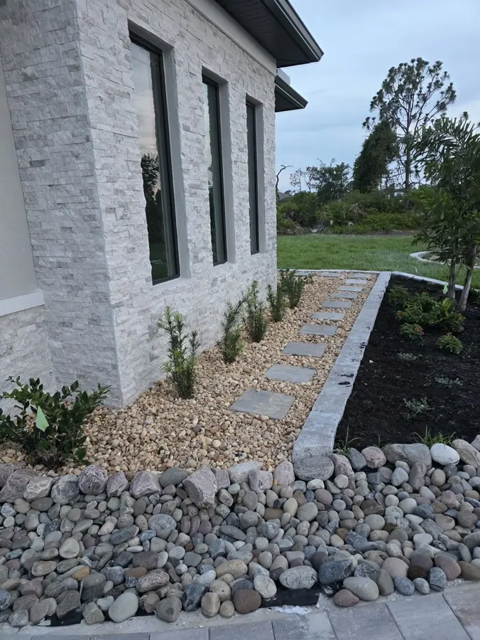 River rock bed with paver stepping stones beside a stacked stone home