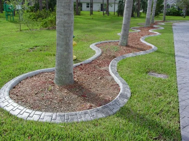 Gray stamped concrete curbing curving around a mulch bed with palm trees next to a stamped concrete driveway