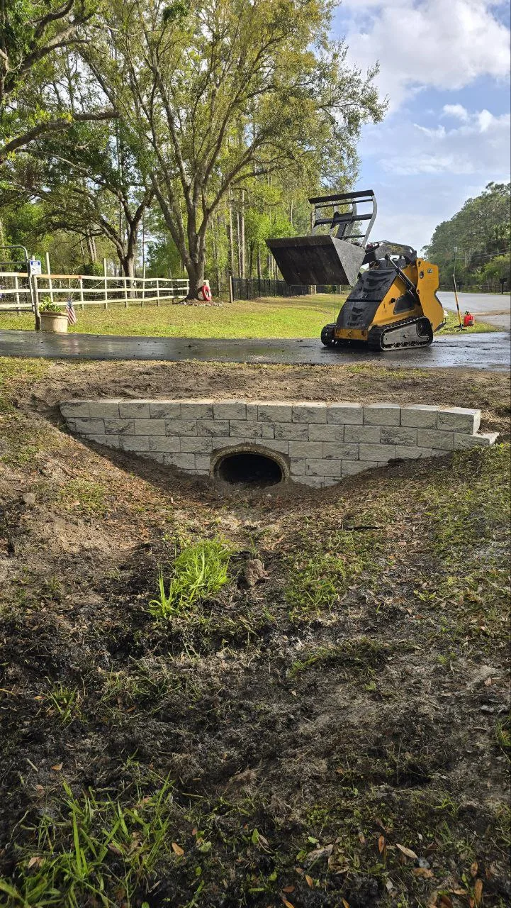 Finished block culvert drainage structure set in excavated earth beside a gravel driveway