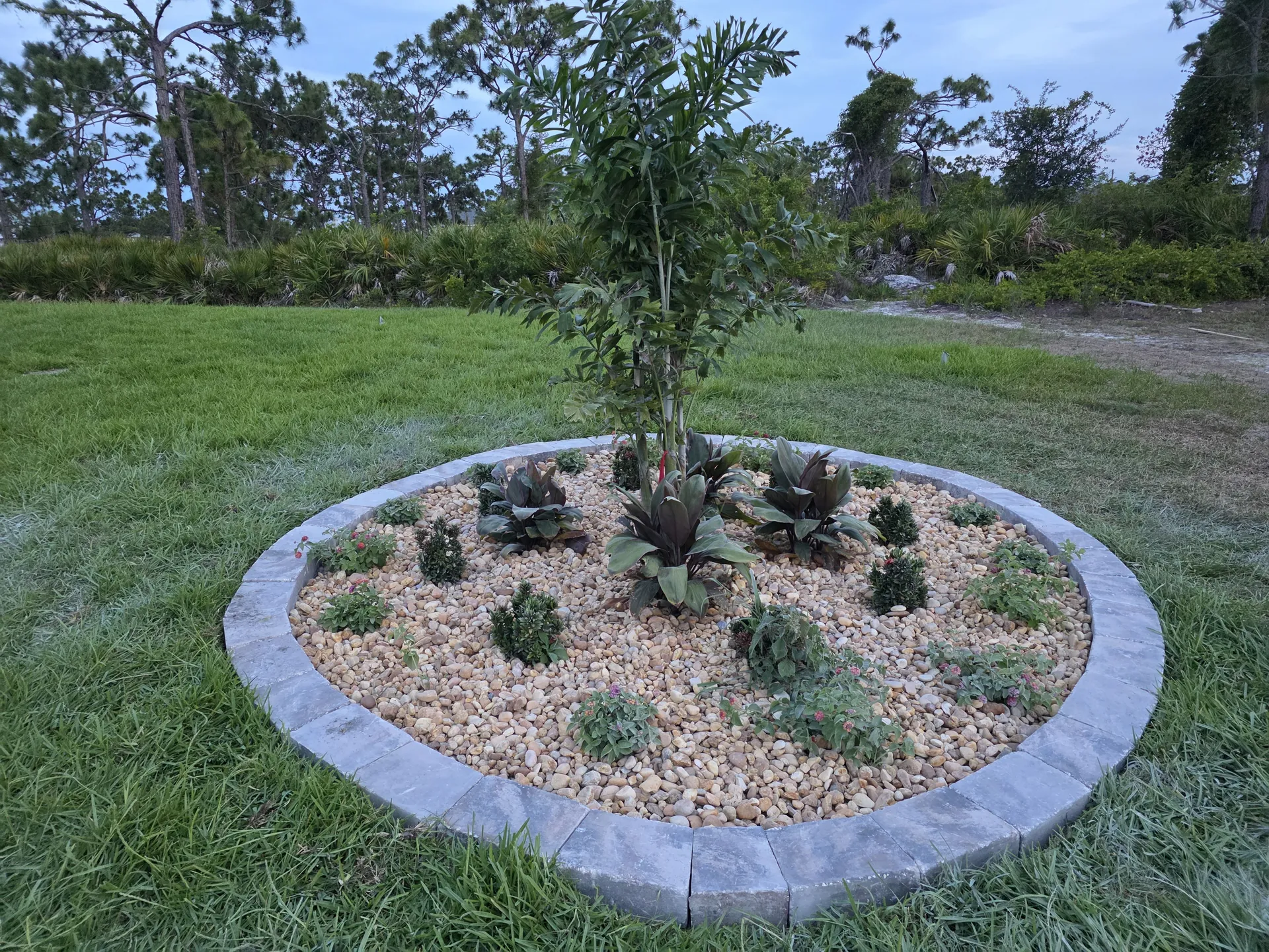 Circular paver-edged island bed filled with decorative rock and plants