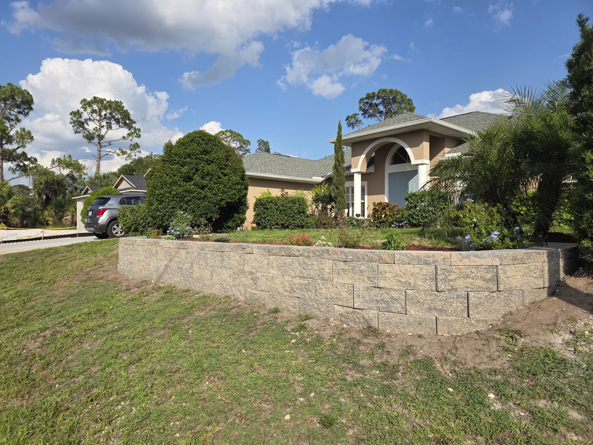 Curved tan block retaining wall with capstones holding a raised front-yard planting bed at a Southwest Florida home
