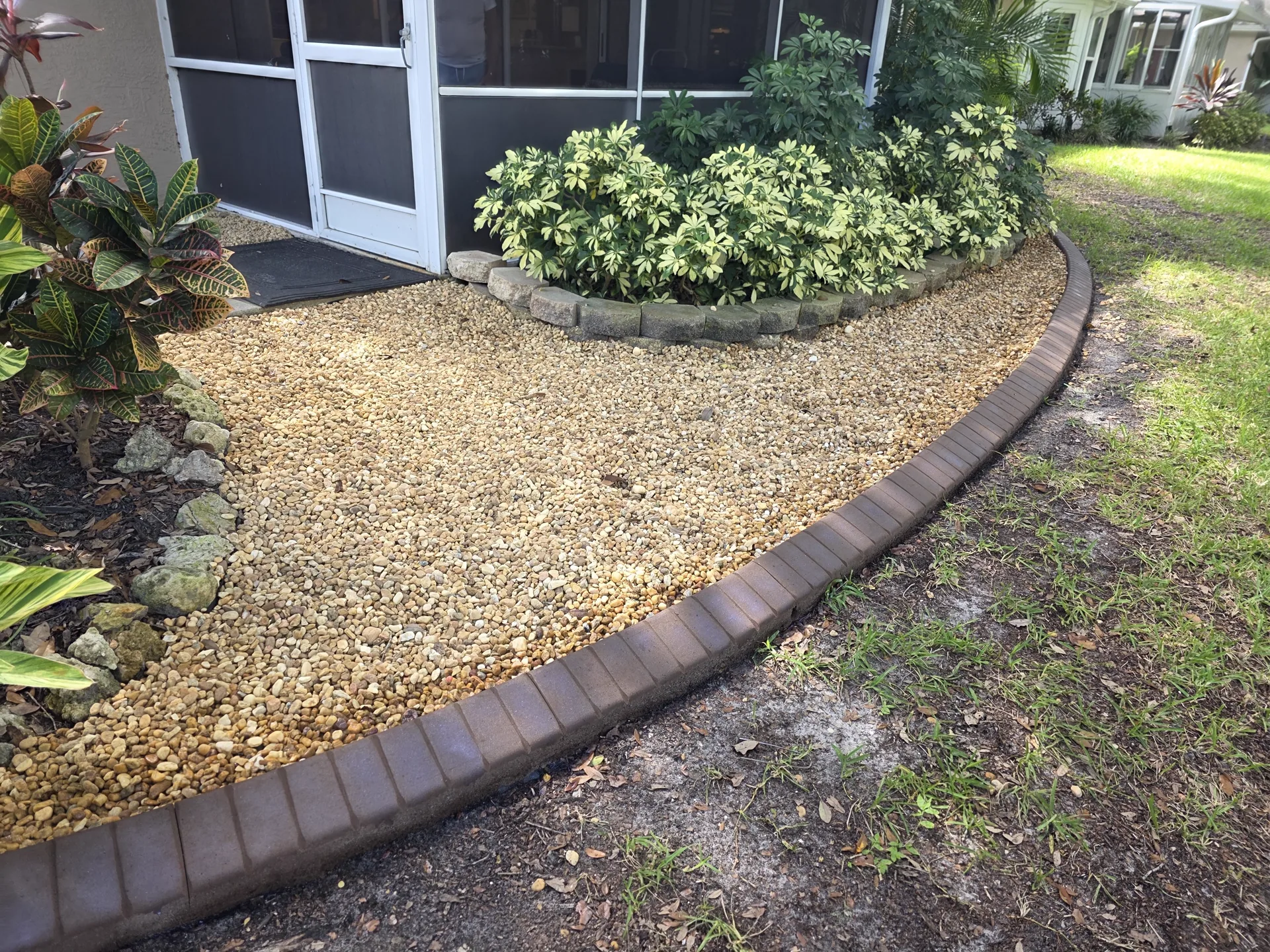 Worker kneeling to hand-stamp fresh concrete curbing along a lawn edge