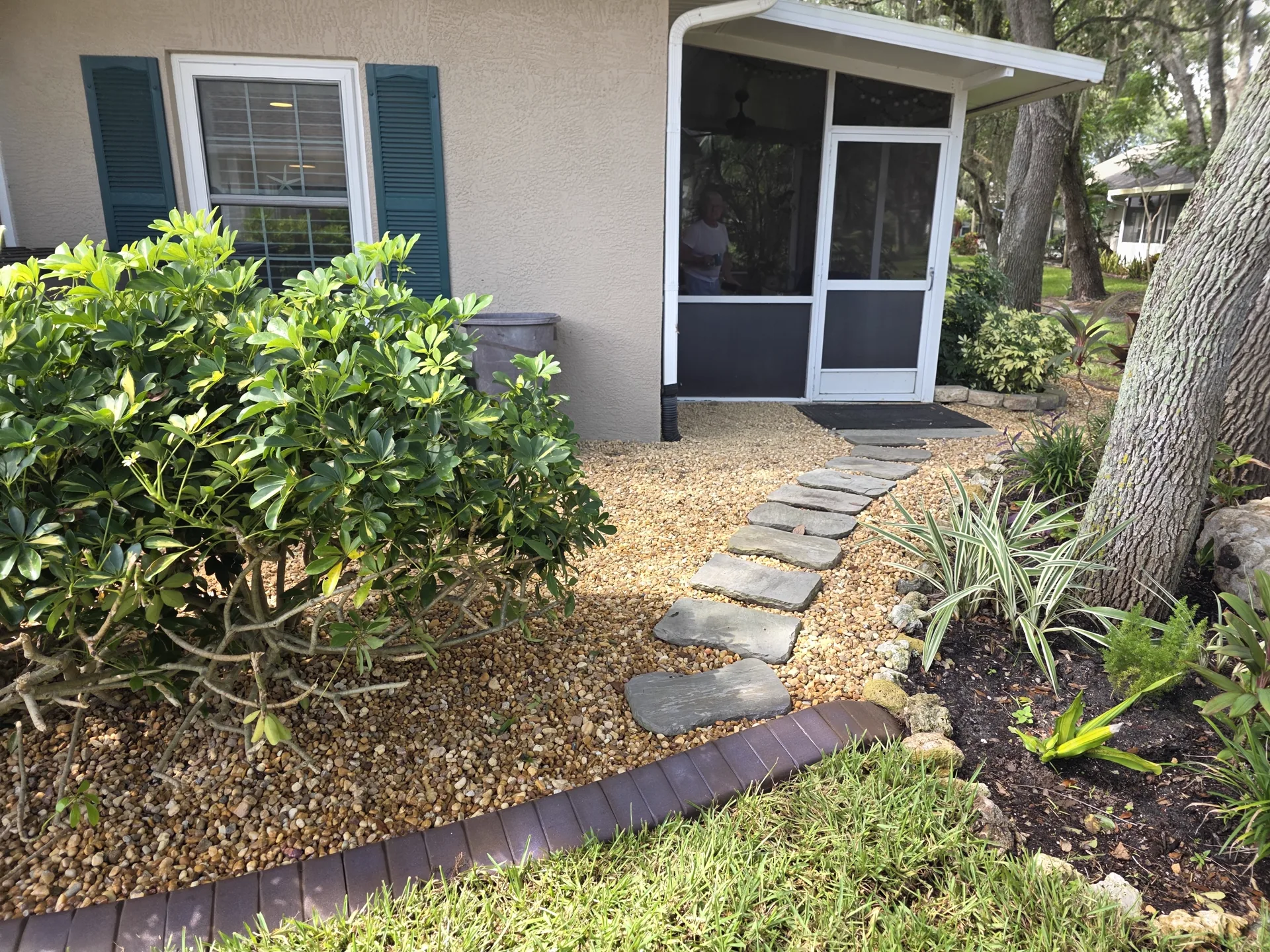 Flagstone stepping stones crossing a pea gravel bed edged with concrete curbing, leading to a screened side entry