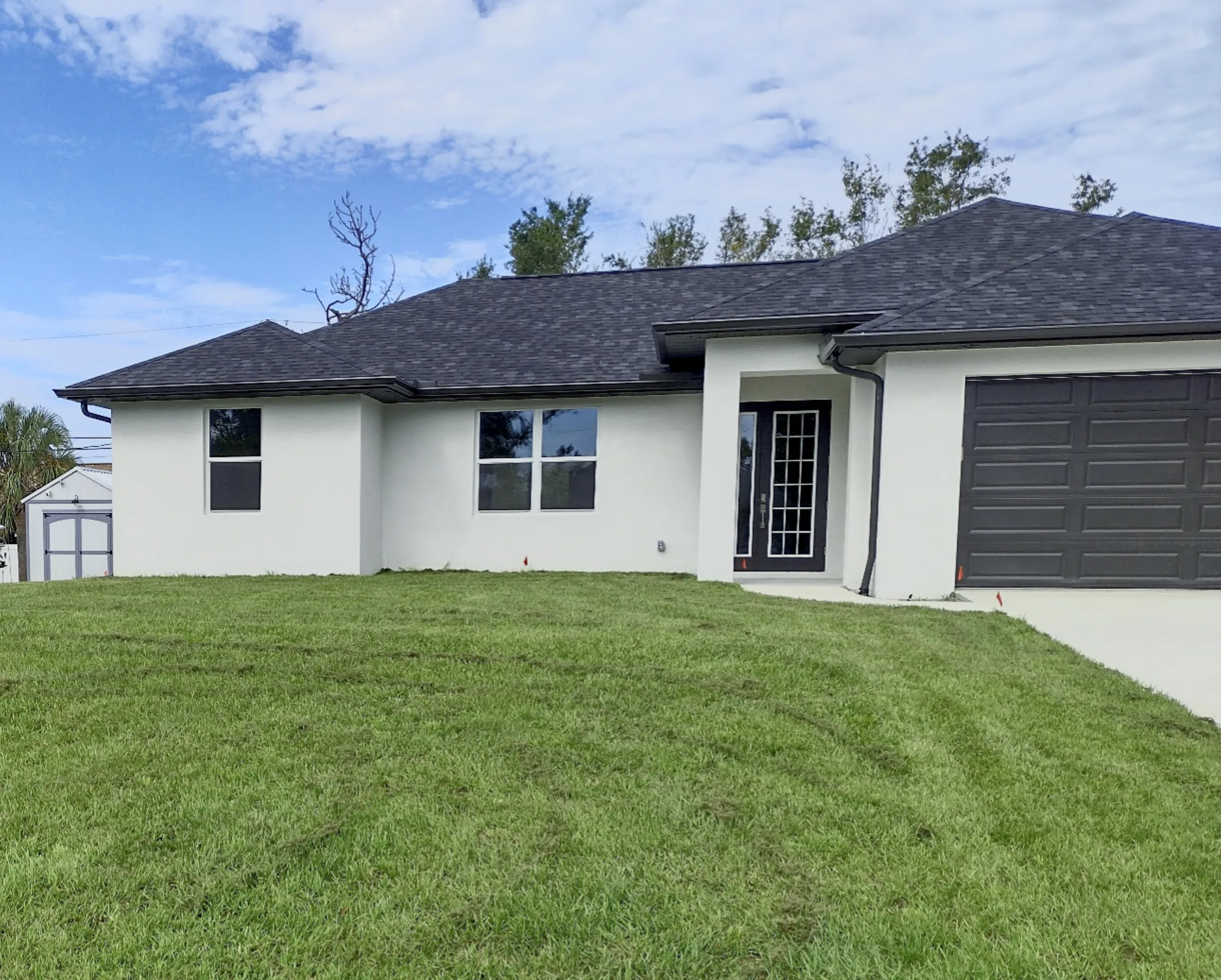 Fresh sod front lawn installed at a new white stucco home with a dark roof and concrete driveway