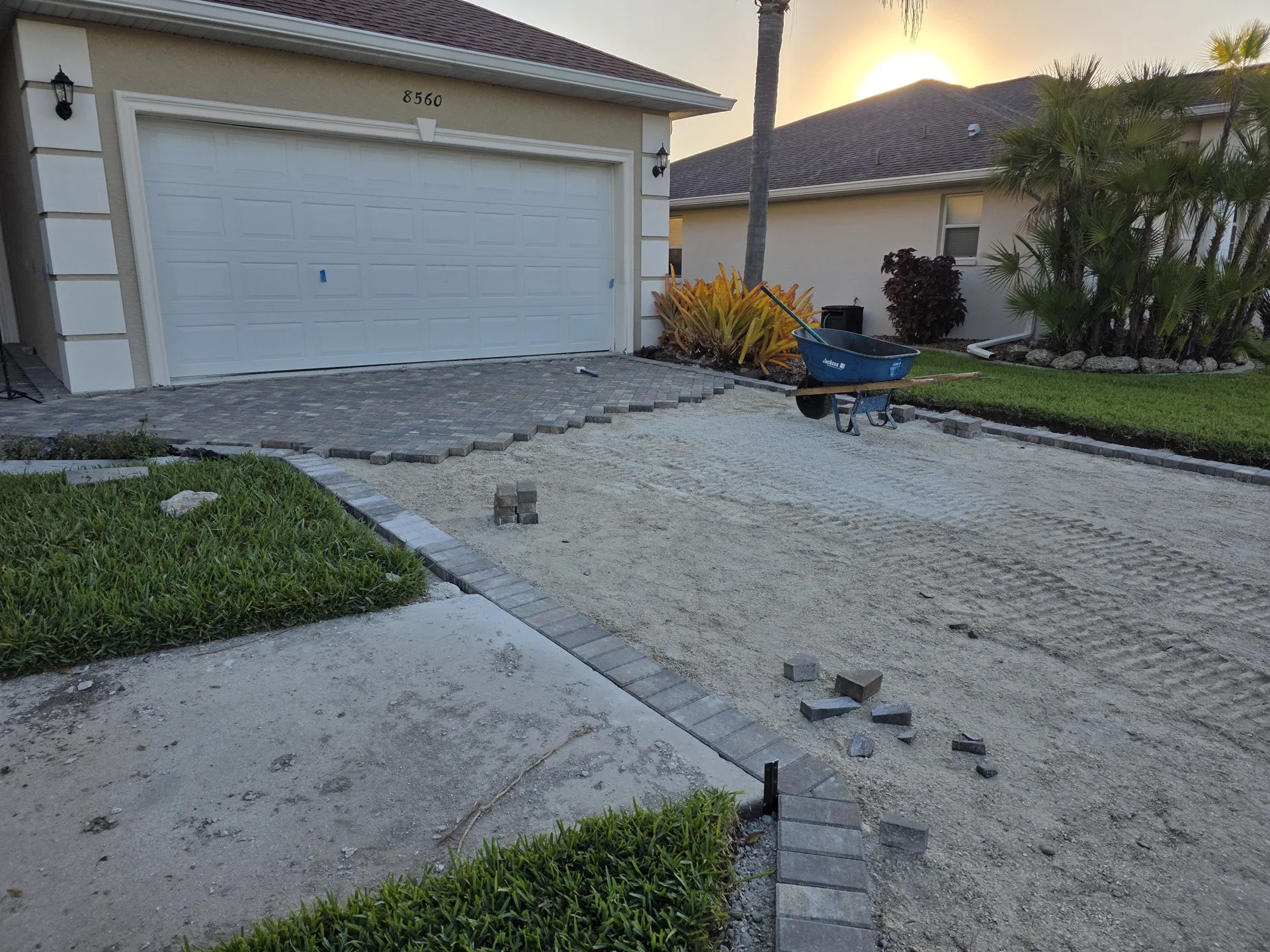 Paver installation in progress at dusk with compacted sand base and staged paver blocks